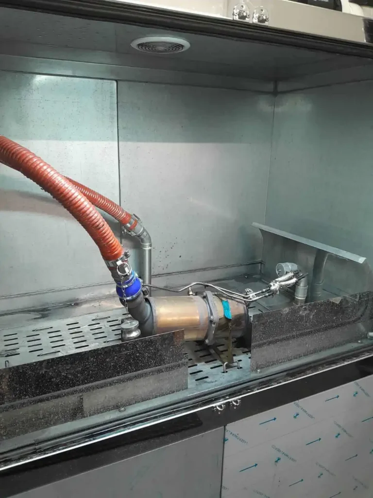 Ausgebauter Partikelfilter mit blauem Adapter und rotem Schlauch in der Reinigungskammer
