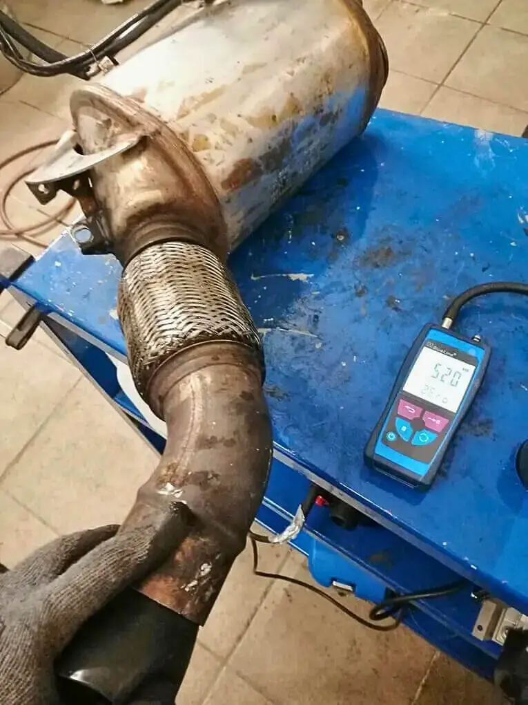 Ausgebauter BMW-3er-Partikelfilter neben einem Druckmessgerät