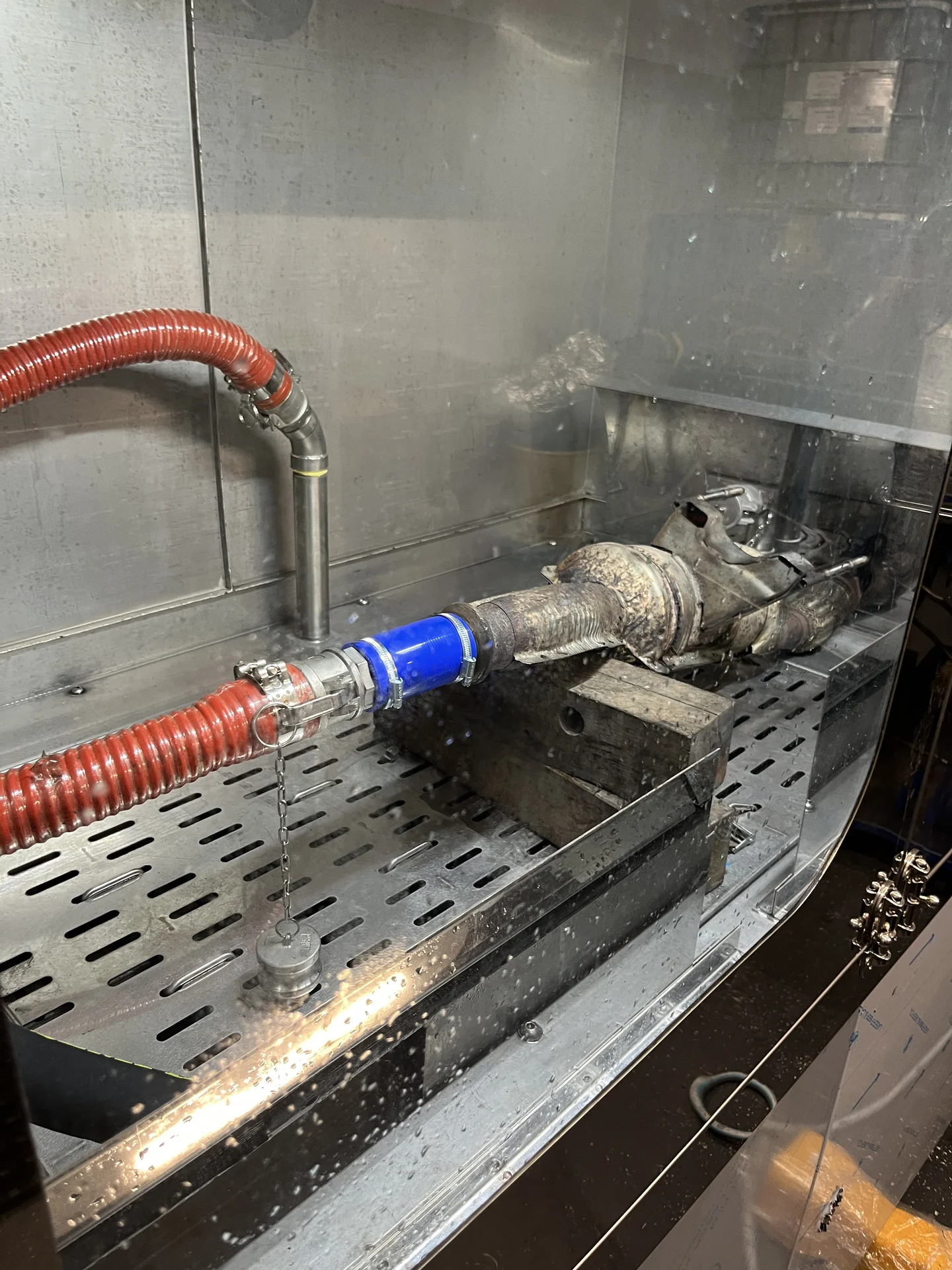 Ausgebauter Dieselpartikelfilter mit angeschlossenem Reinigungsschlauch in einer Edelstahlkabine.